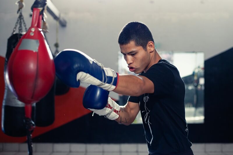 Man with blue gloves punching a bag