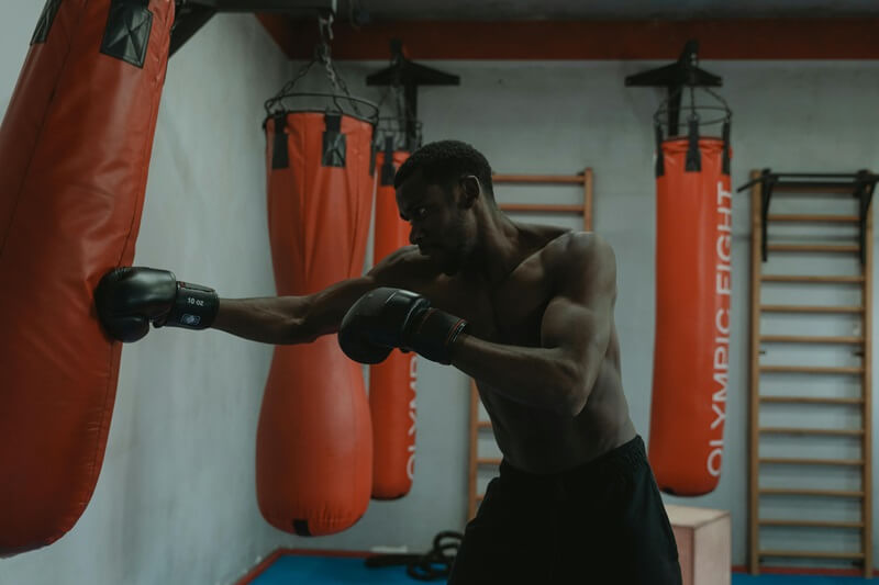 Shirtless man with black gloves punching red punching bag